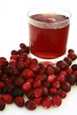 glass with red drink surrounded by a pile of cranberries